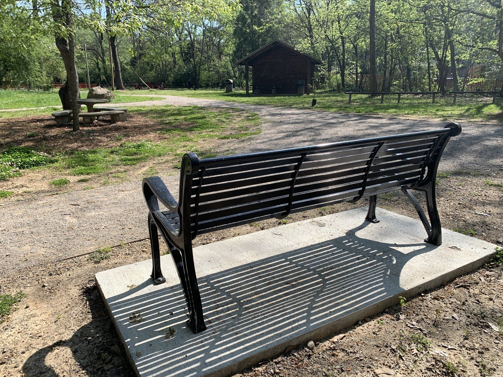A black bench is sitting on a concrete platform in a park.