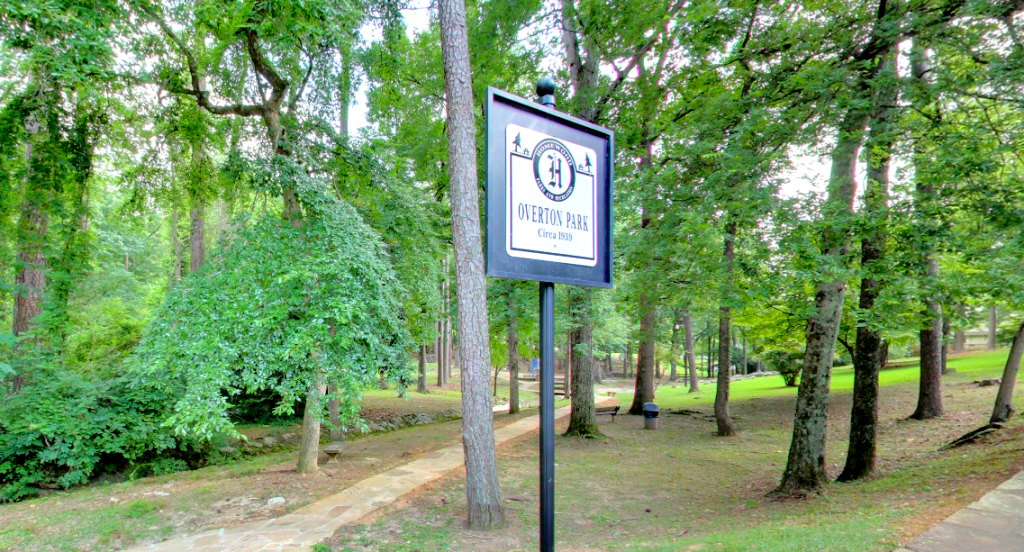 A sign in the middle of a park with trees in the background.