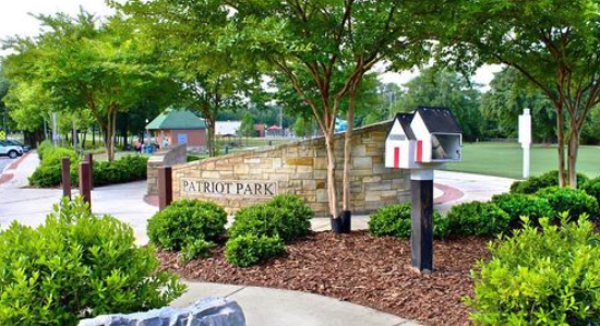 A sign for patriot park is surrounded by trees and bushes.