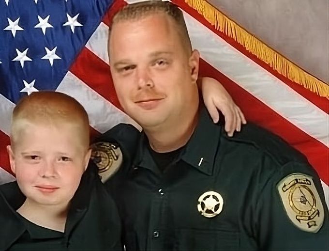 a man in a sheriff 's uniform is posing with a boy in front of an american flag
