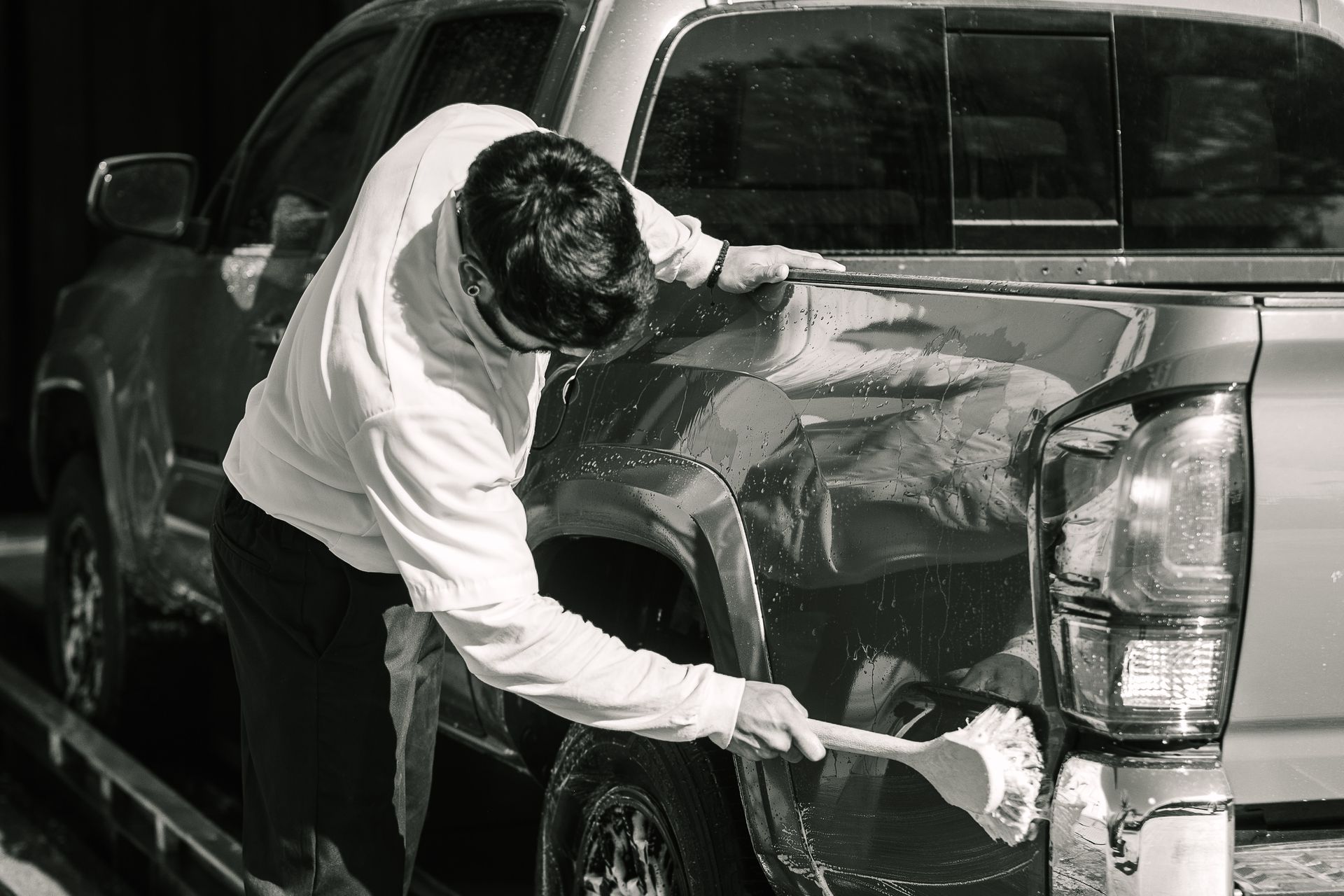 A man is cleaning the side of a truck with a brush.