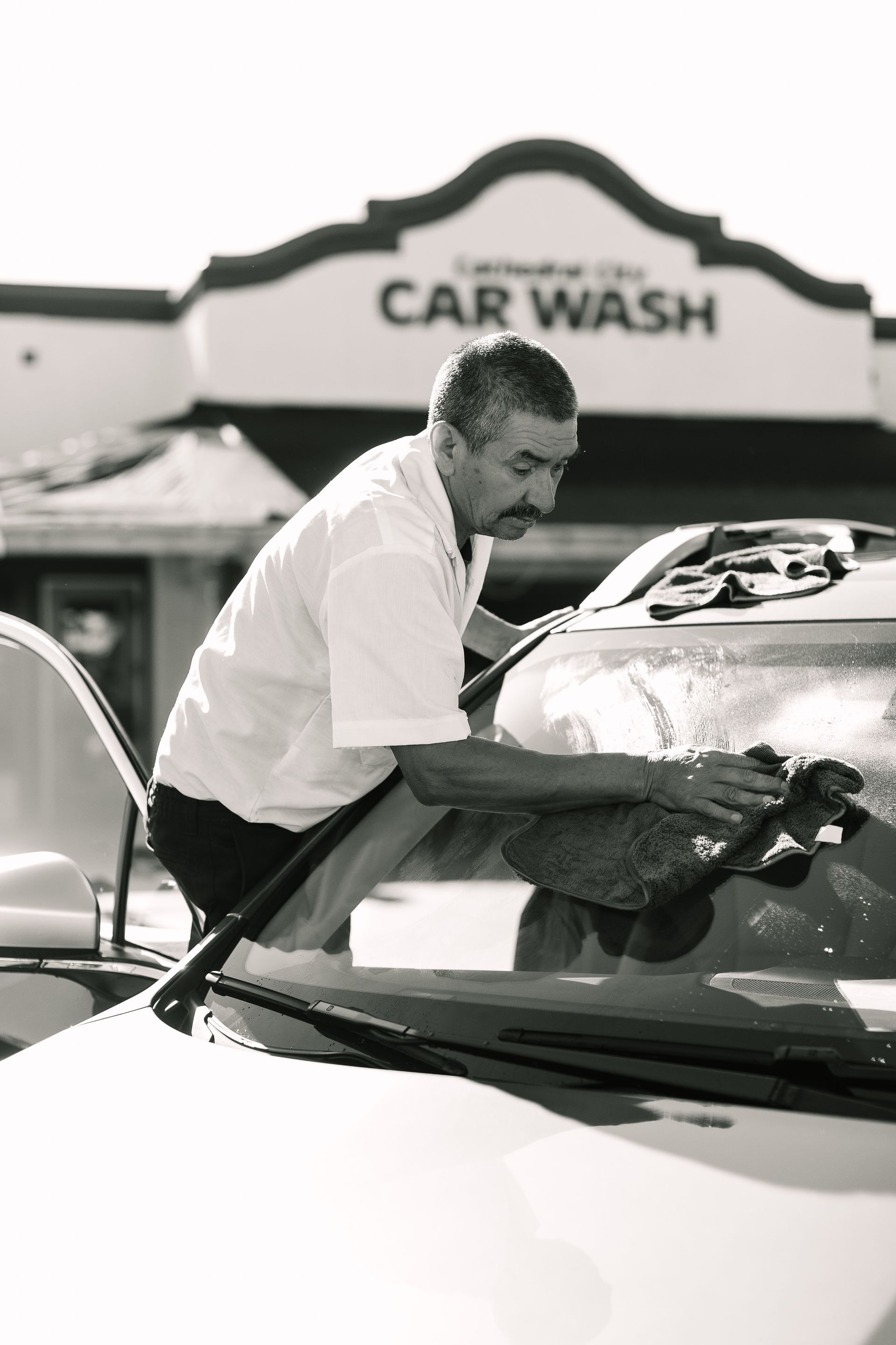 A man is cleaning the windshield of a car in front of a car wash