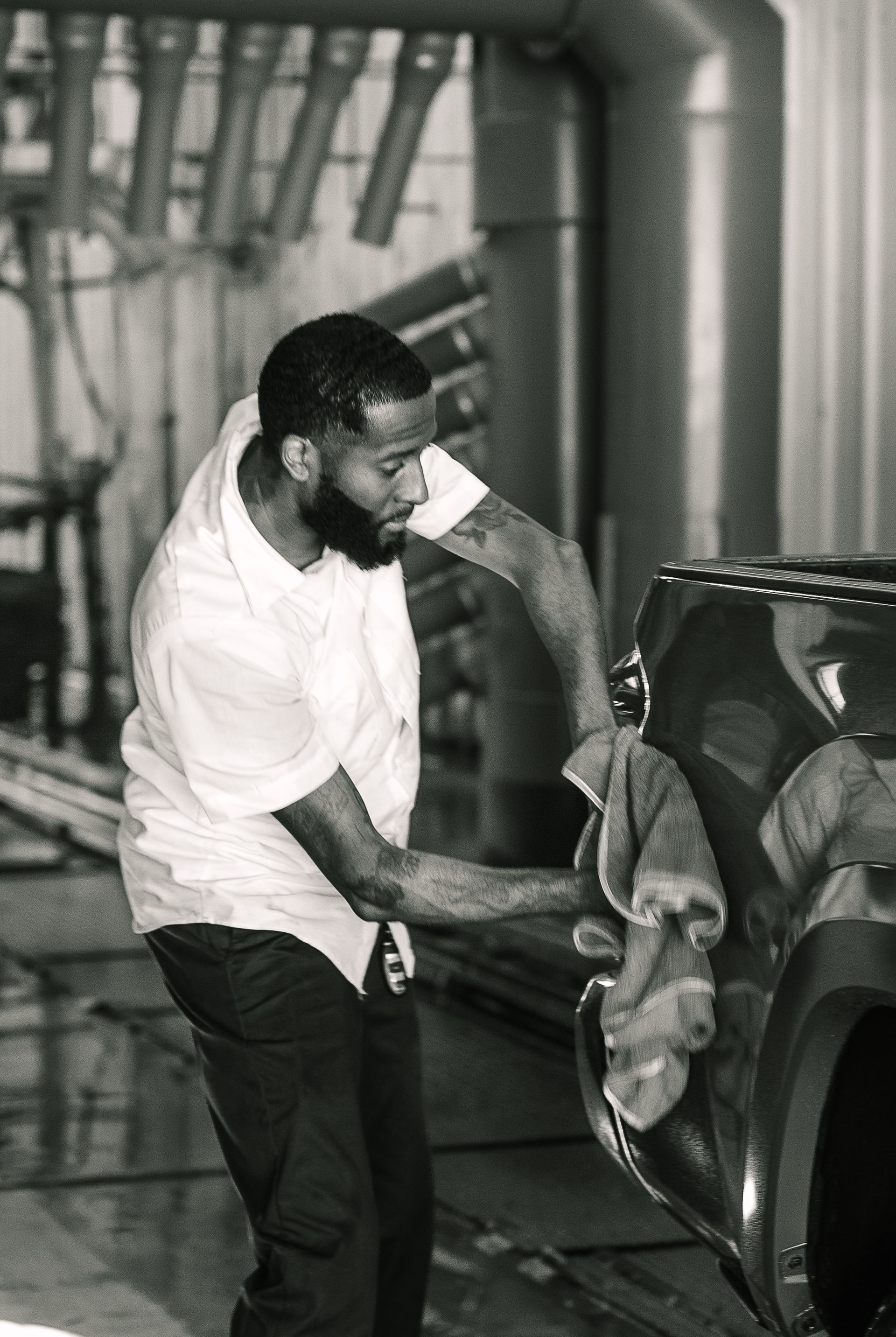 A man is cleaning a car with a towel in a black and white photo.