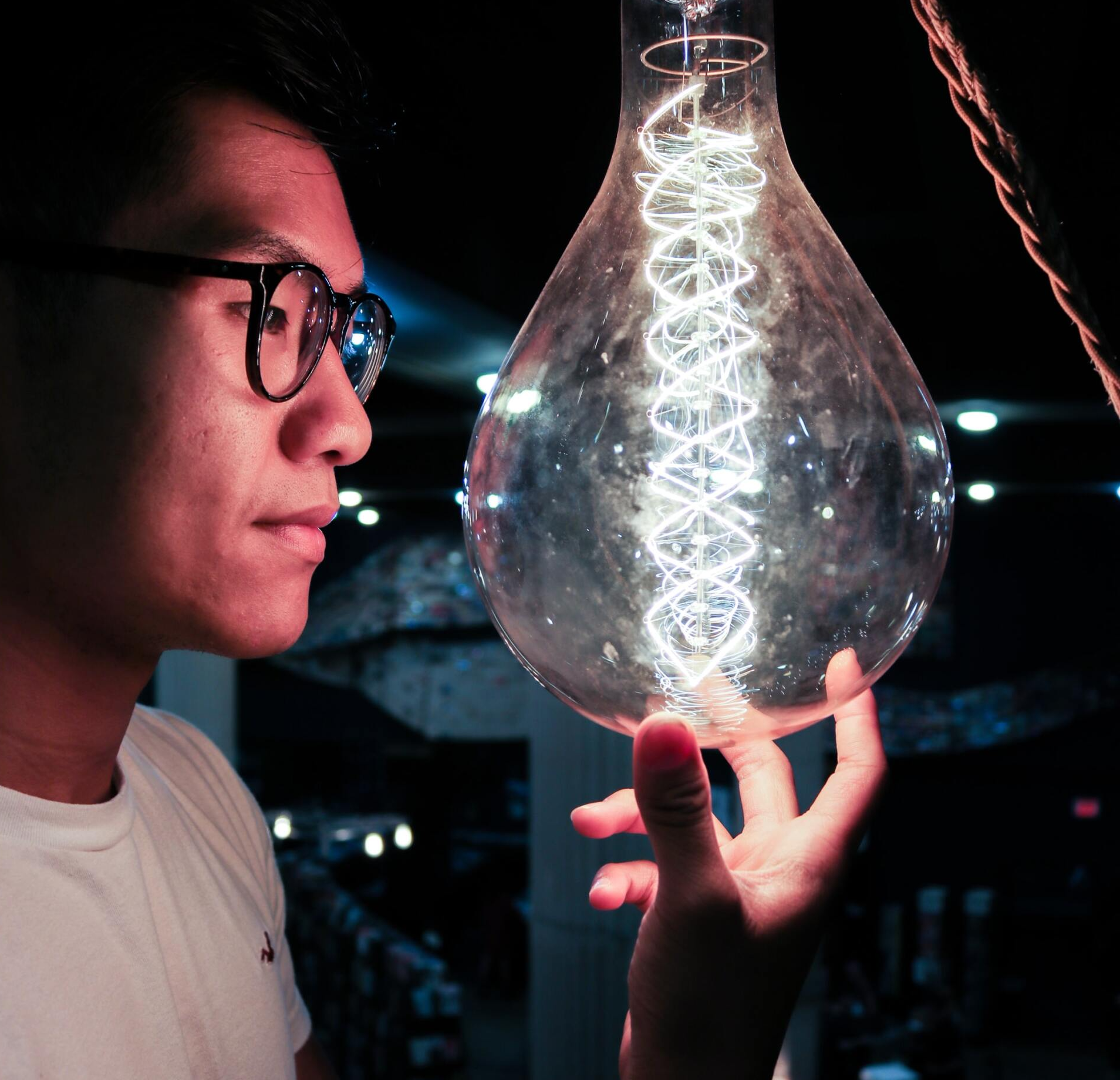 A man wearing glasses is holding a light bulb in his hand