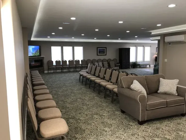 Empty waiting room with rows of chairs, a couch, wall TV, and large windows
