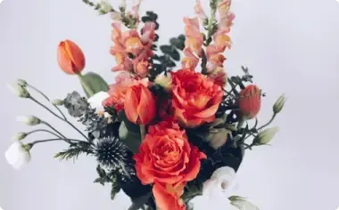 Bouquet of orange and pink flowers with greenery in a white vase