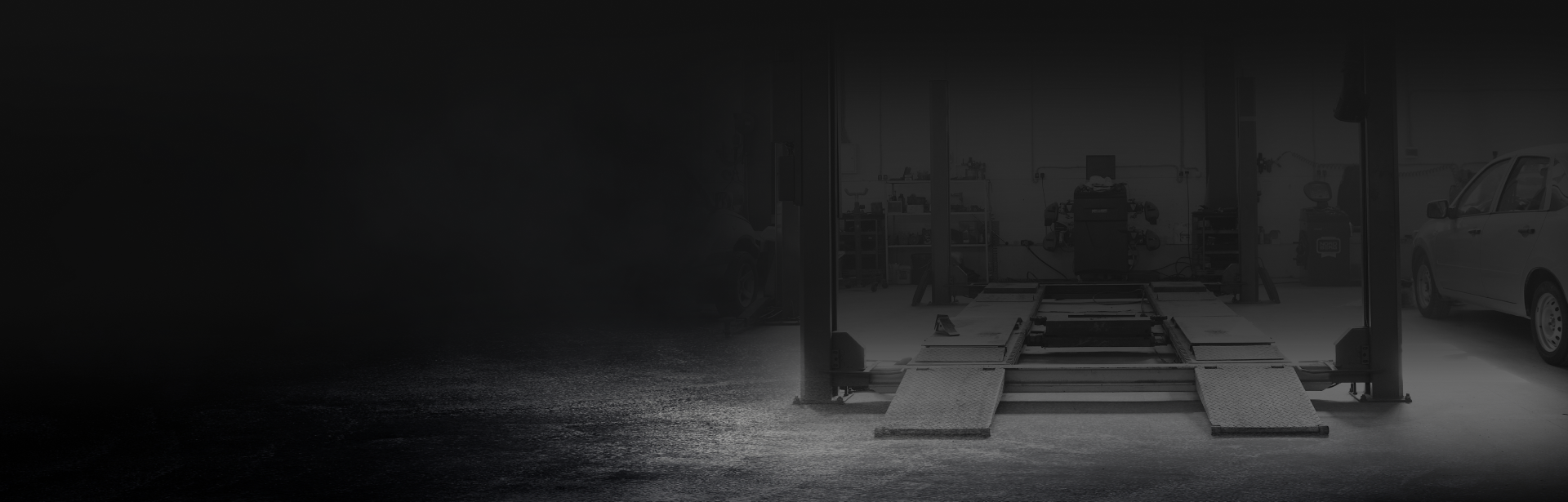 Auto repair shop with car on lift, worker in background. Black and white, grungy. | ECP Auto Service