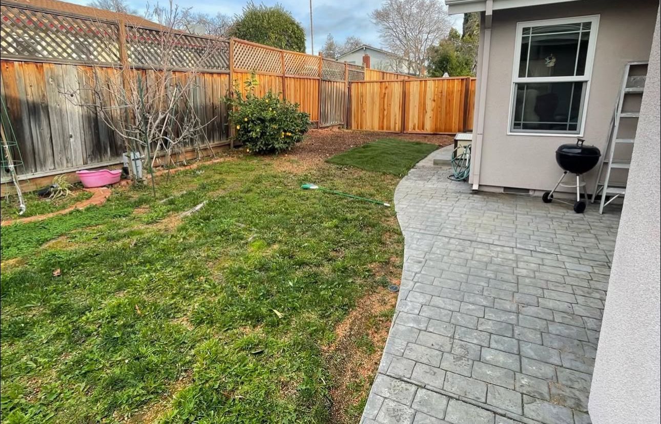 A backyard with a fence and a patio with a grill