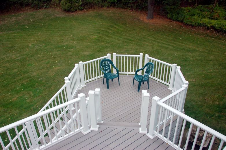 A deck with two green chairs and a white railing
