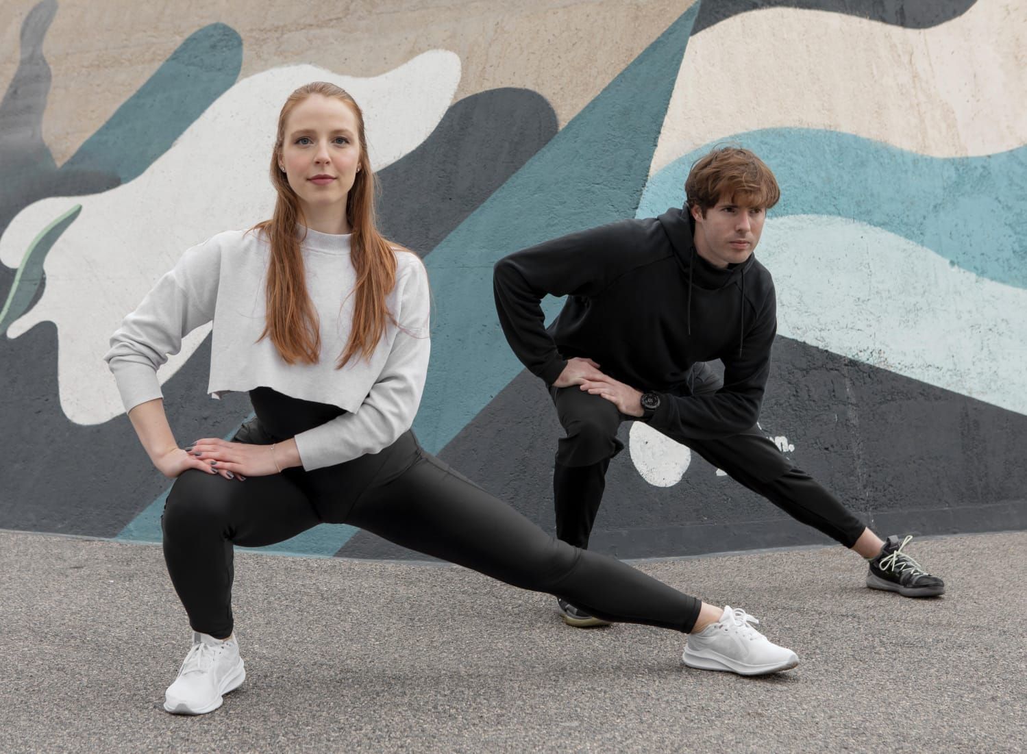 Mujer y hombre haciendo zancadas laterales frente a una pared pintada.