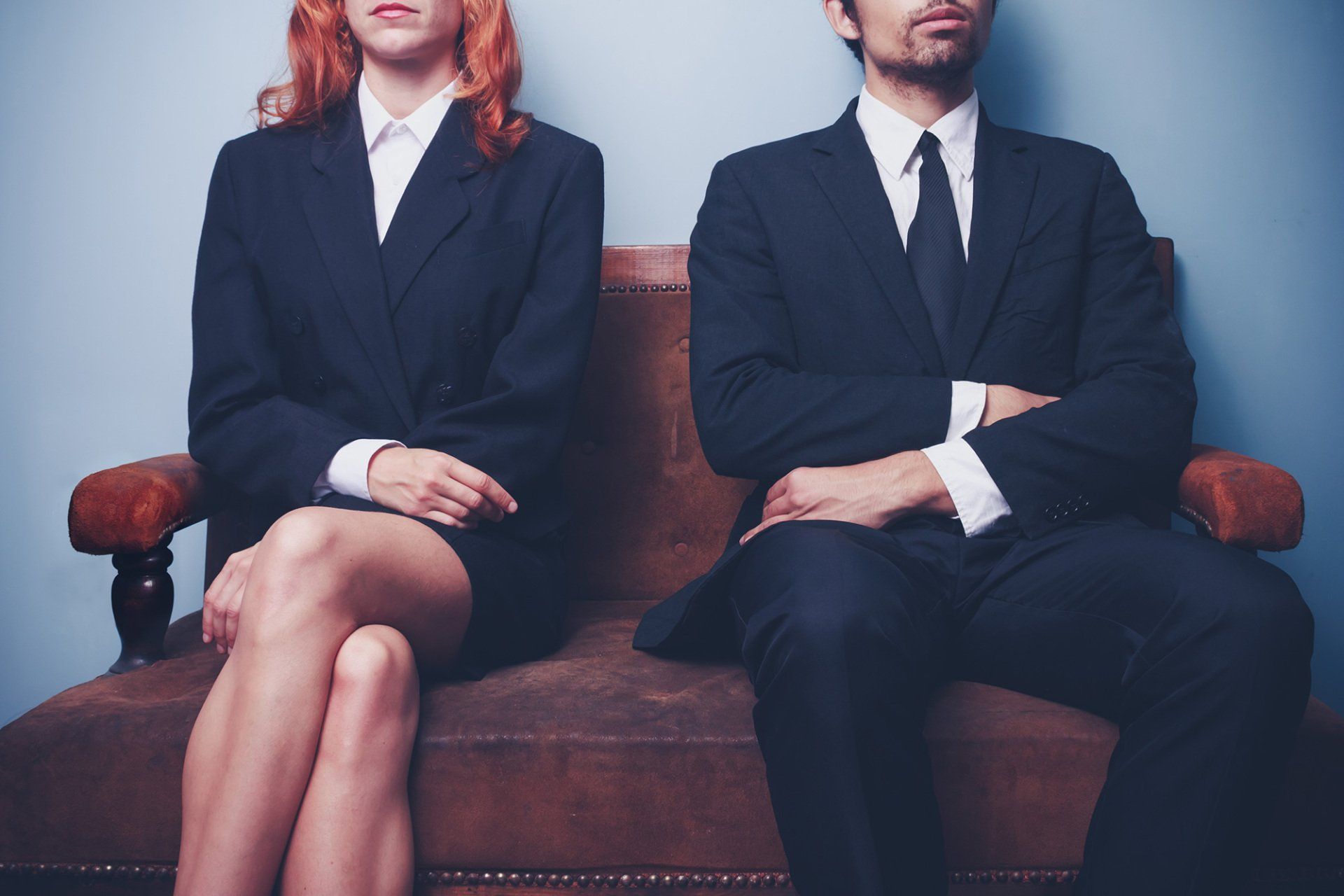 Two sharply dressed business people are waiting on a sofa with a serious expression on their faces