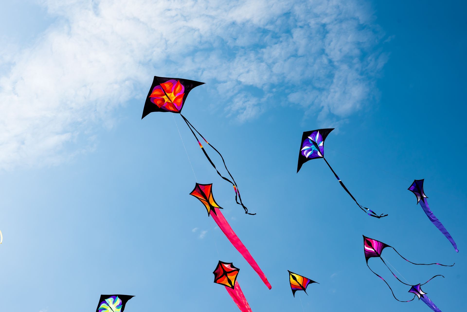 Colourful kites flying high up against a blue sky