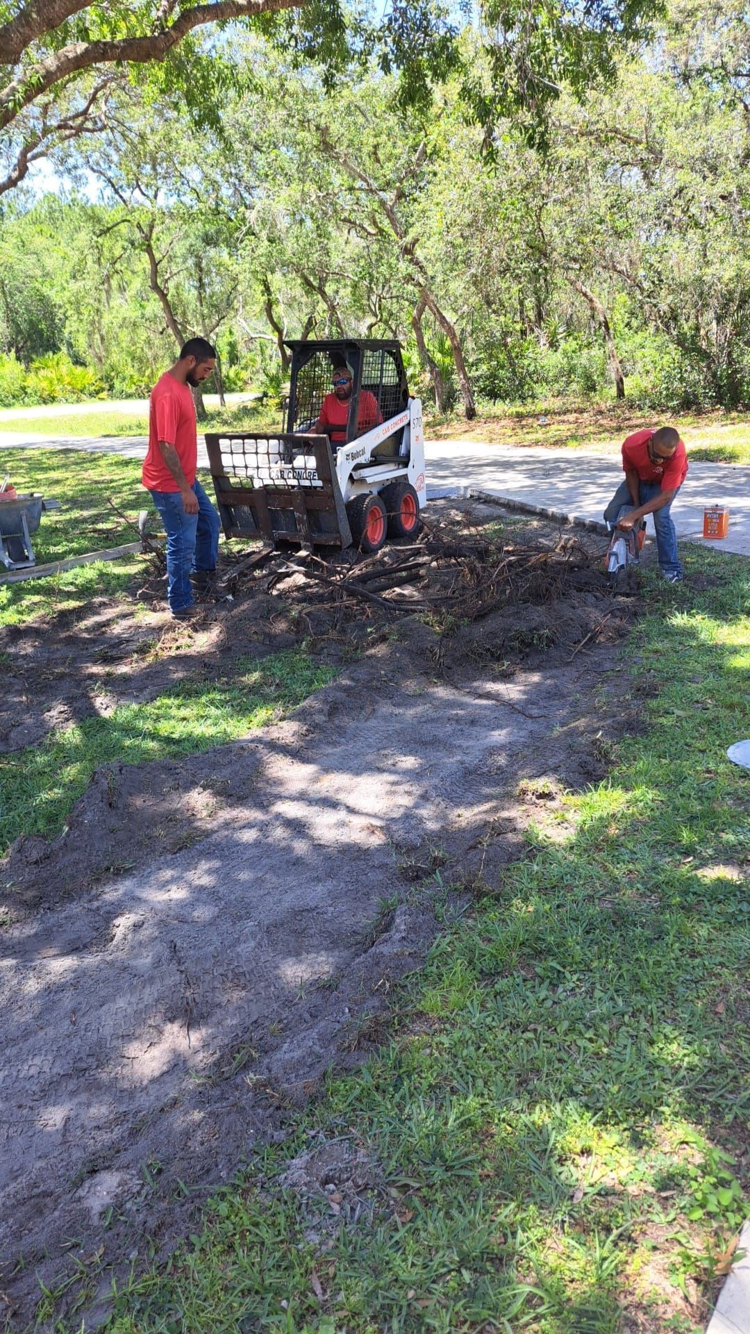 Two men are working on a dirt road next to a bobcat.