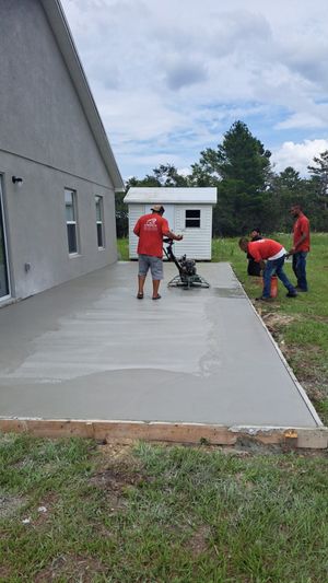 A group of men are working on a concrete driveway in front of a house.