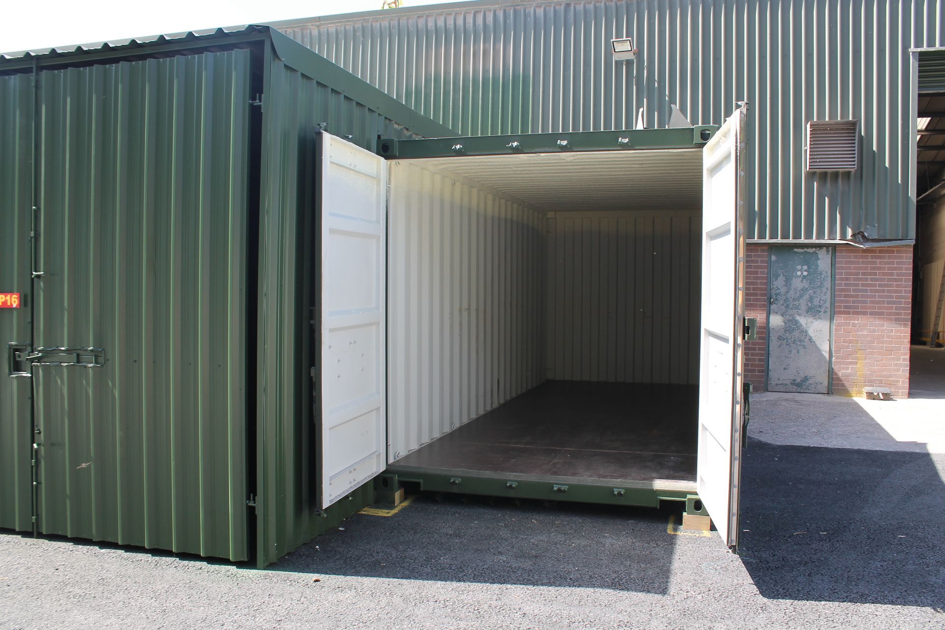 Open green shipping container with white double doors, showing an empty interior on gravel.