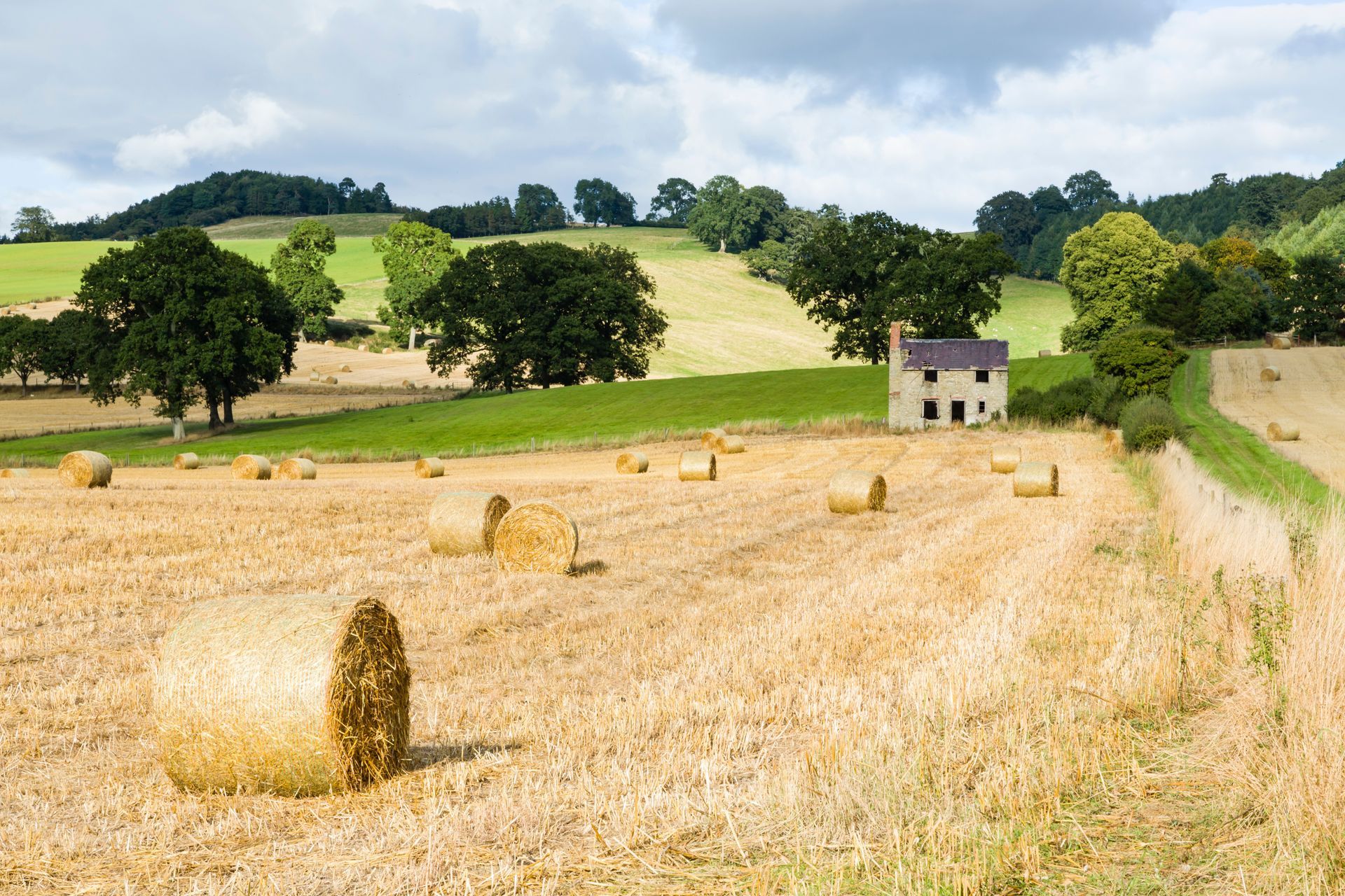 Image of hay field with rolled bails of hay near old farmouse building by rolling green hills near Oswestry in Shropshire, England