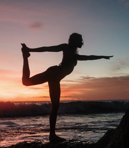 A woman is doing yoga on the beach at sunset.