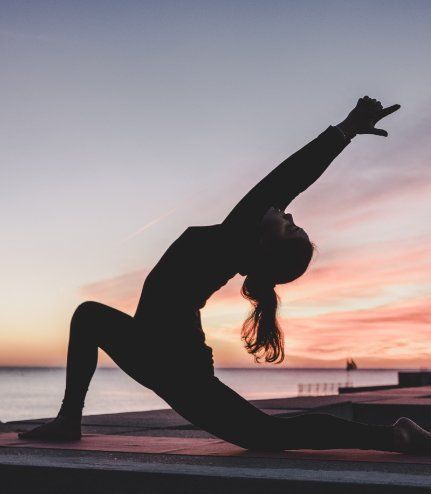 A silhouette of a woman doing yoga on a beach at sunset