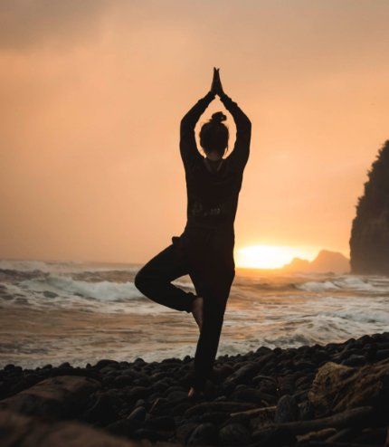 A woman is practicing yoga on the beach at sunset
