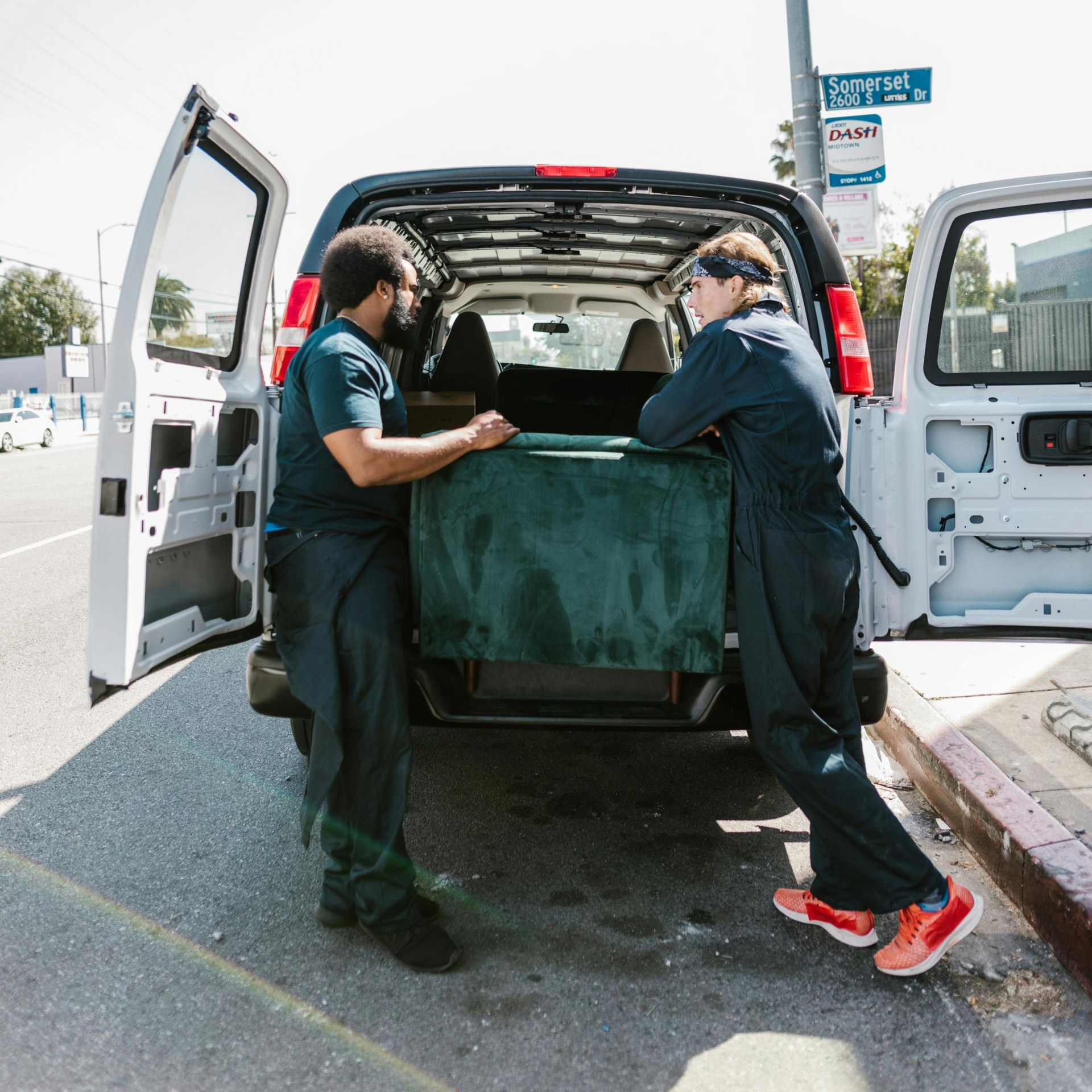 Two workers in safety gear opening a cargo container, using long bars. One wears orange, the other white.