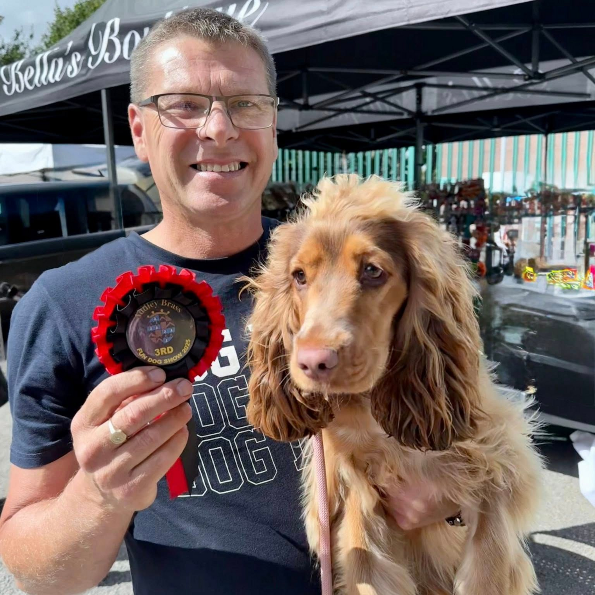 Jon, a member of the Charli's Pet Angels team, holding up a rosette and his cocker spaniel puppy