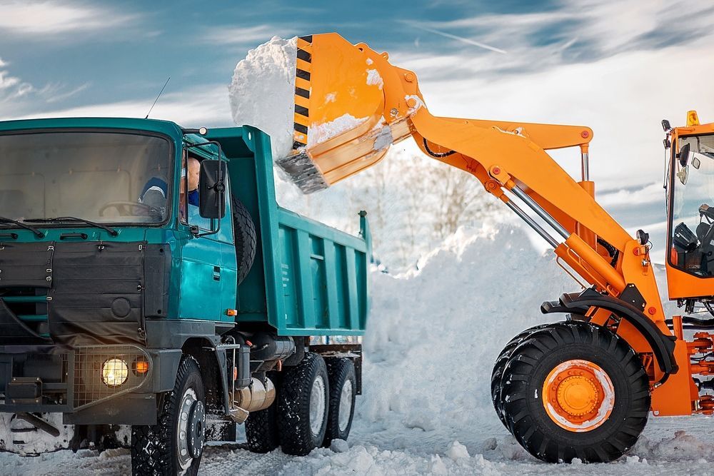 A dump truck is being loaded with snow by a bulldozer.