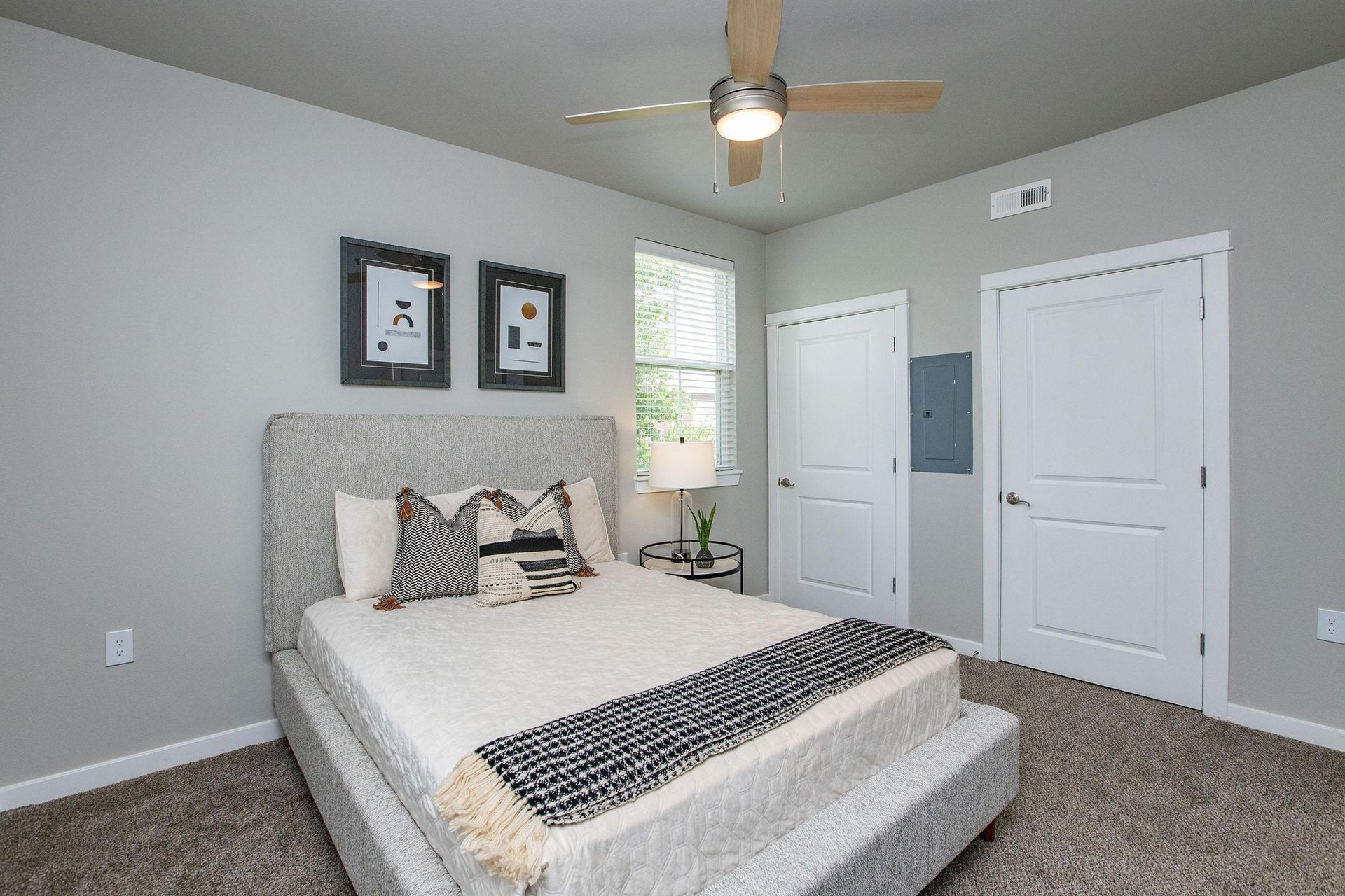 Bedroom with a bed, two doors, a window, artwork, and a ceiling fan.