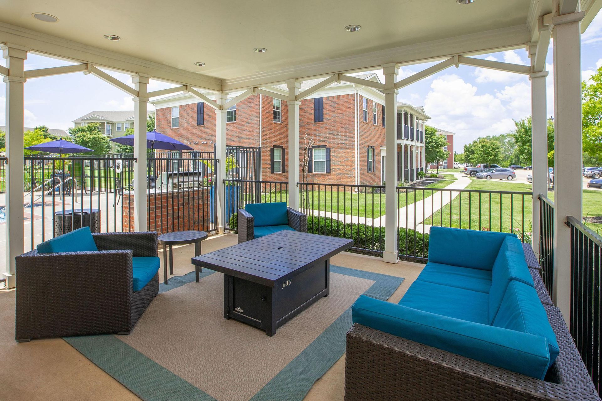 Covered outdoor seating area with blue cushions, a fire pit, and view of brick buildings.