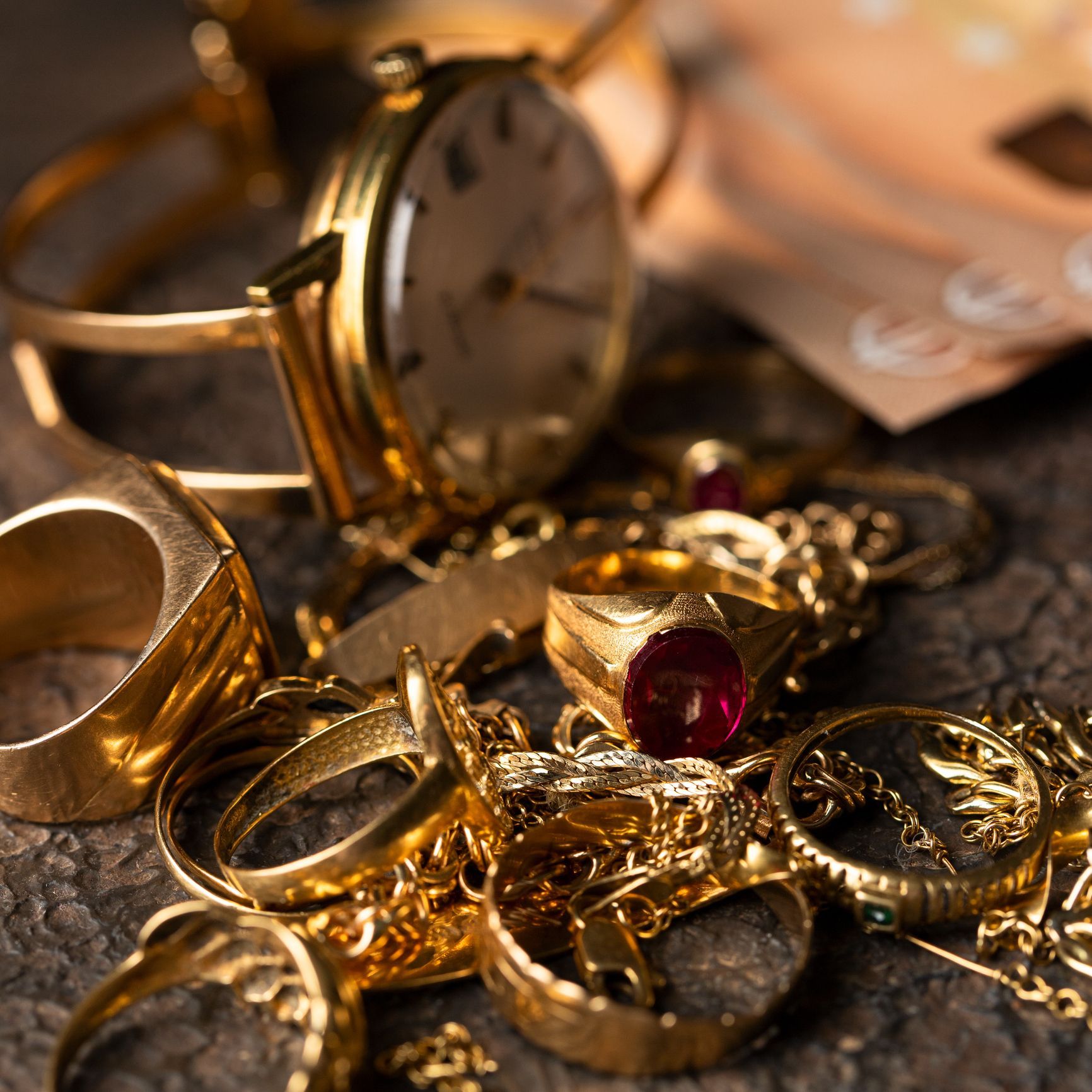 Gold jewelry, including rings, necklaces, and a wristwatch, lies on a rough surface.