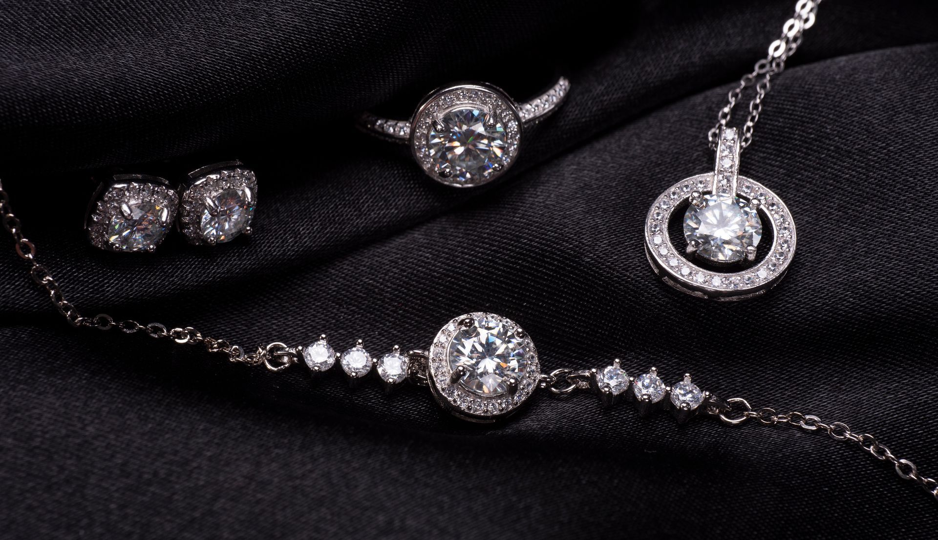 Jewelry set on black fabric: earrings, ring, necklace, and bracelet with diamonds.