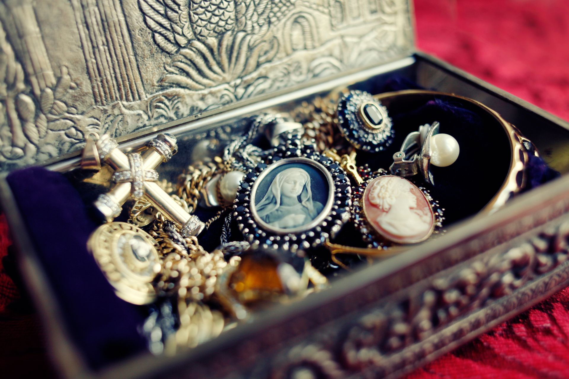 Jewelry box with an ornate silver lid open, revealing a collection of vintage necklaces, bracelets, and rings on a velvet-lined interior.