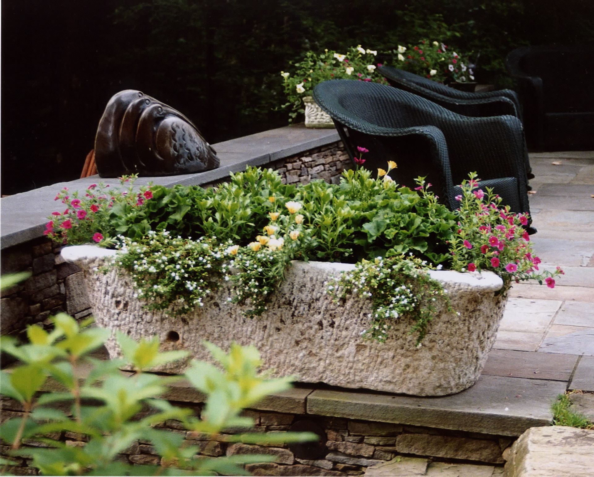 A stone planter filled with flowers sits on a stone patio