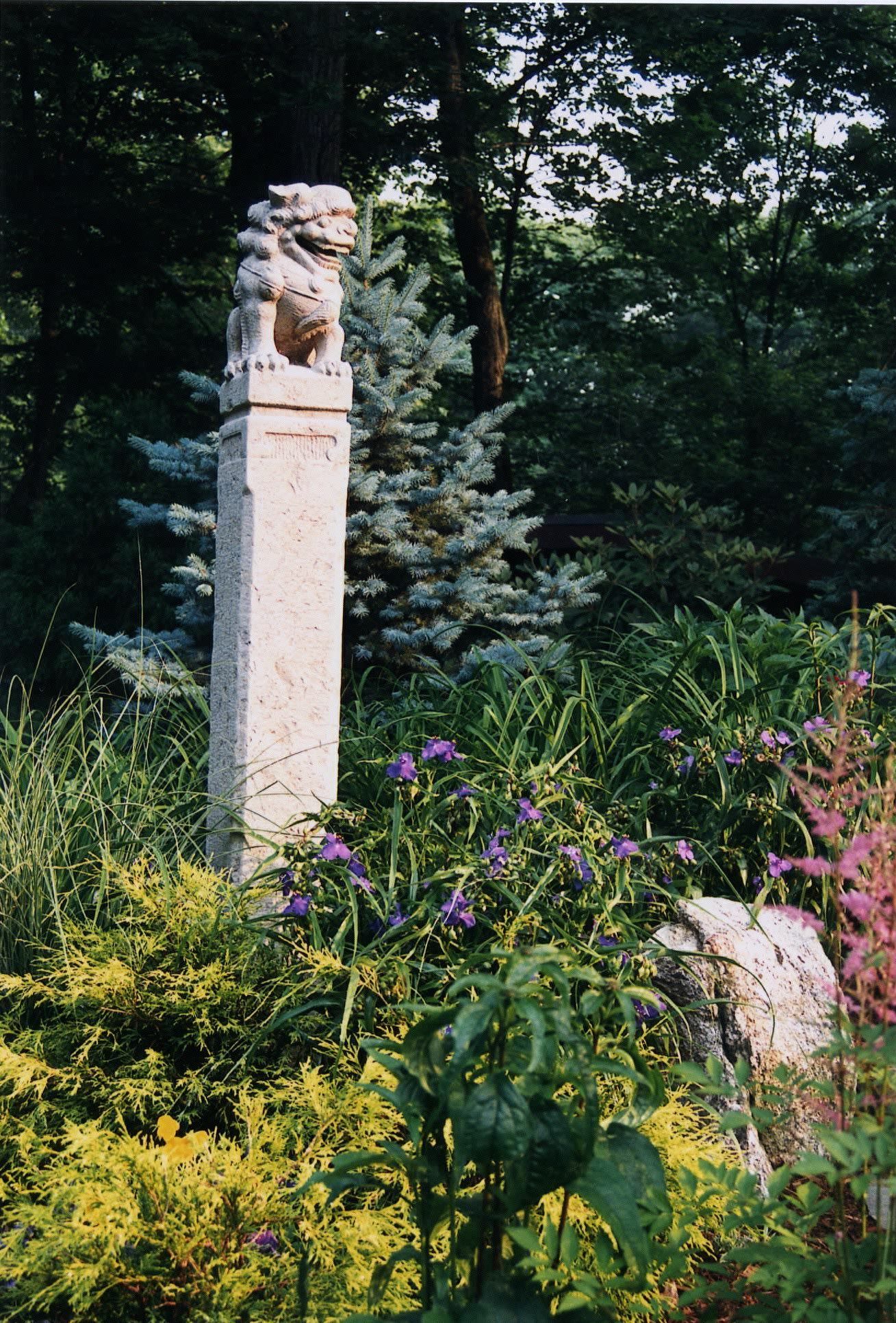 A statue of a lion on top of a pillar in a garden