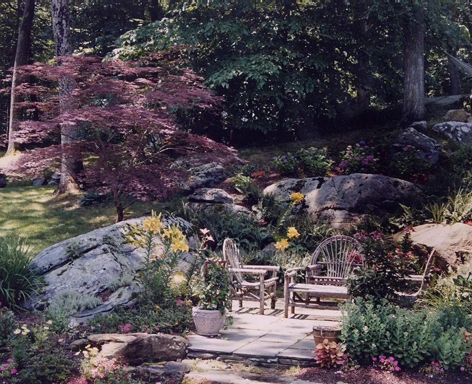 A garden with a bench and chairs surrounded by rocks and flowers