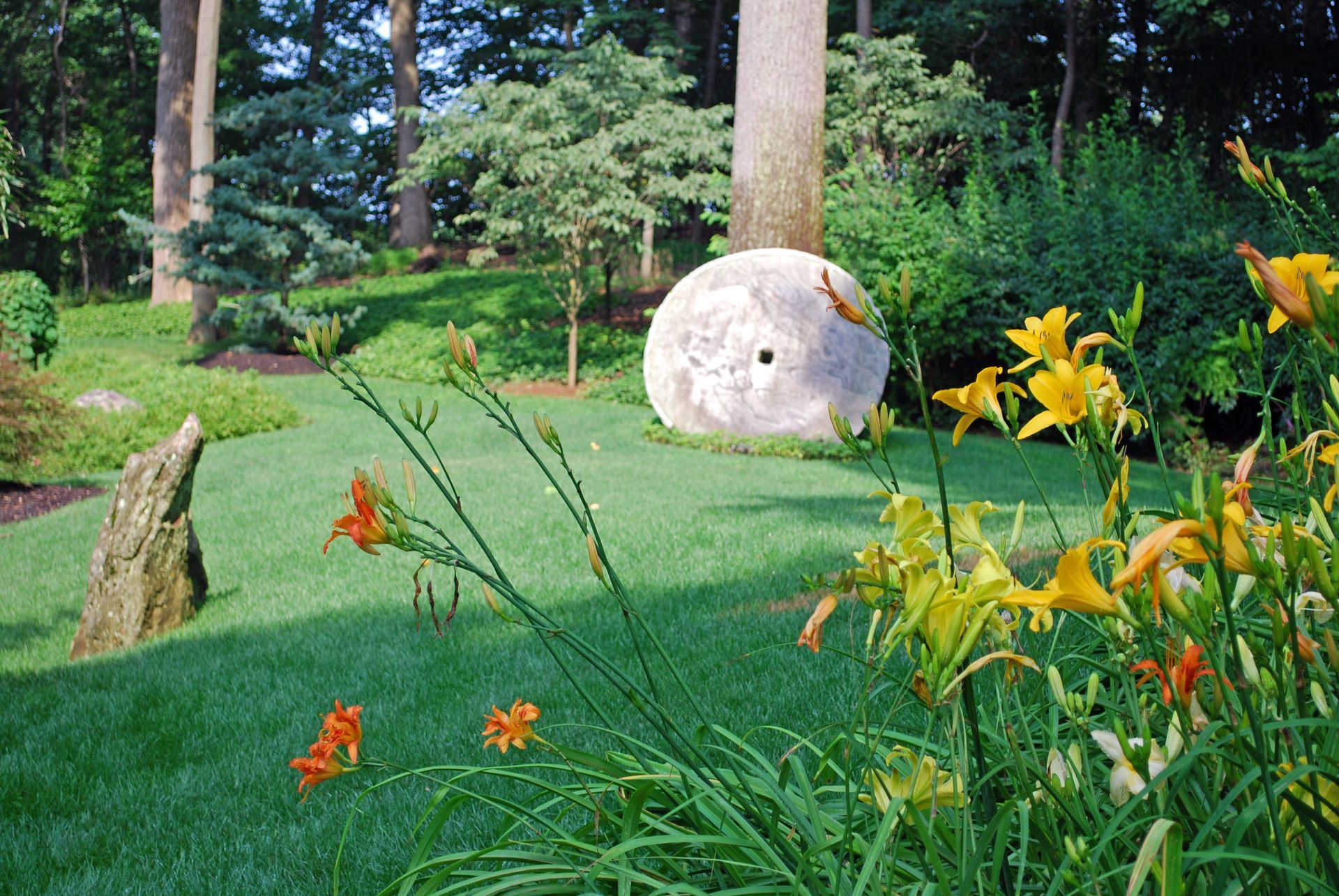 A large rock is sitting in the middle of a lush green field surrounded by flowers.