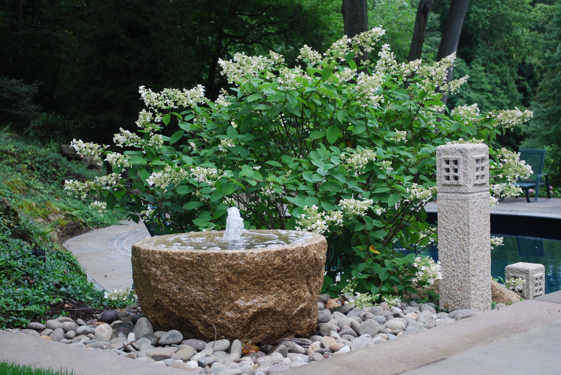 A fountain in the middle of a garden next to a tree