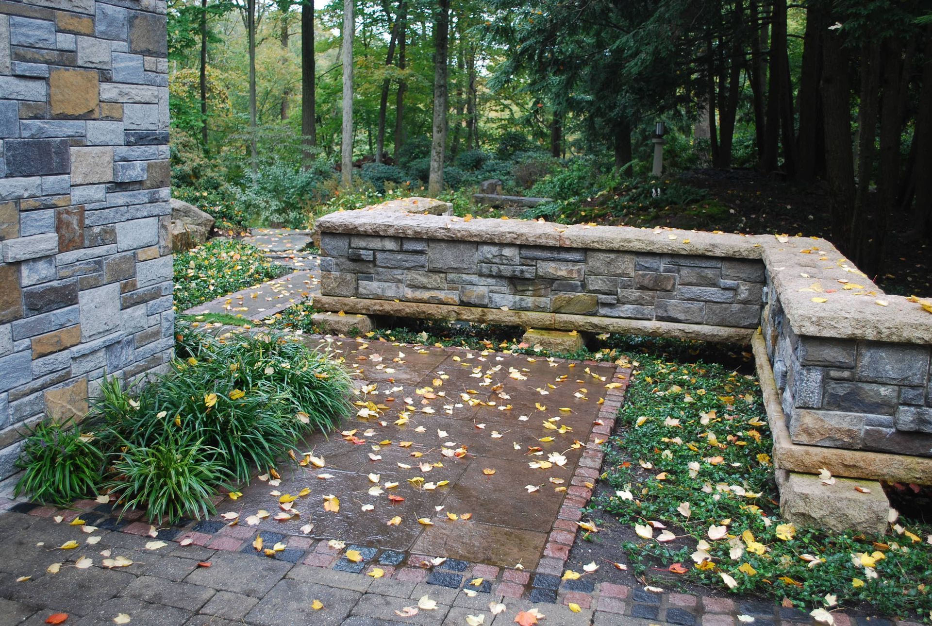 A stone wall surrounds a brick walkway in the woods