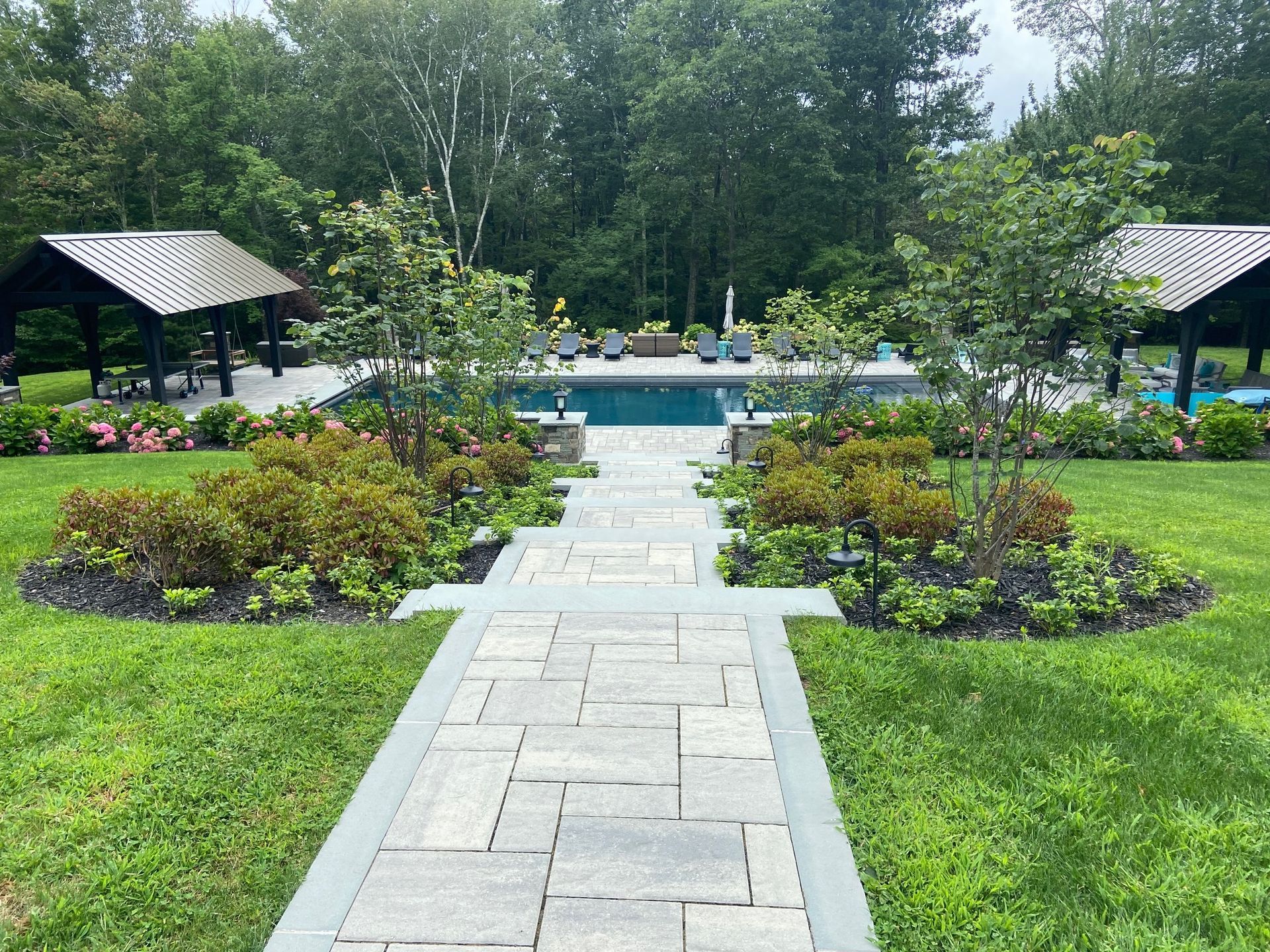 A walkway leading to a large swimming pool in a backyard.