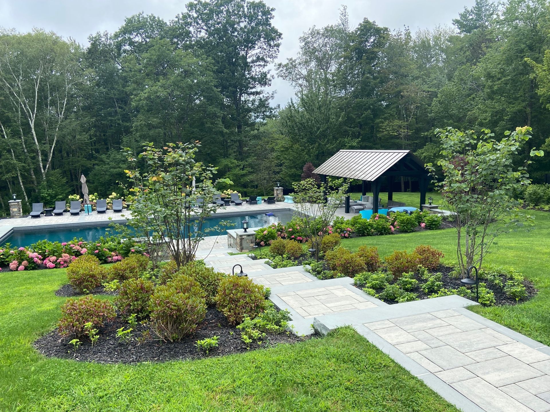 A large swimming pool is surrounded by a lush green lawn and trees.