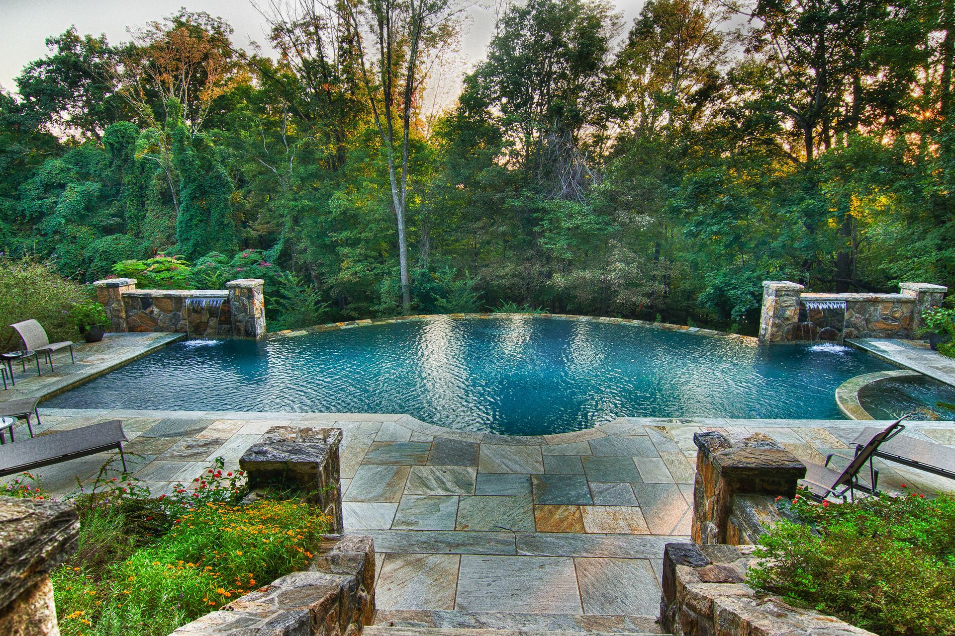 A large swimming pool is surrounded by trees and a stone patio.