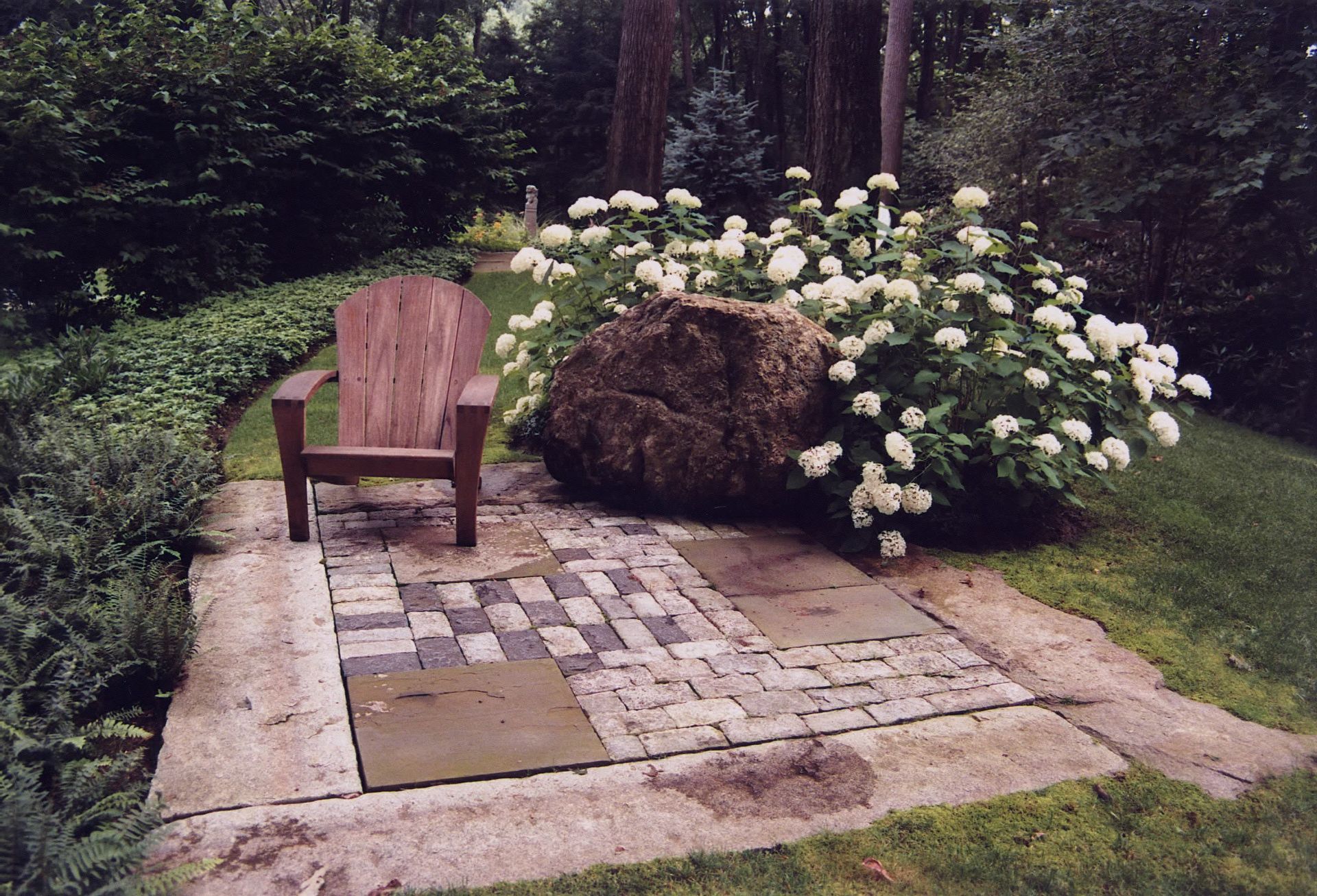 A wooden chair sits on a stone patio in a garden