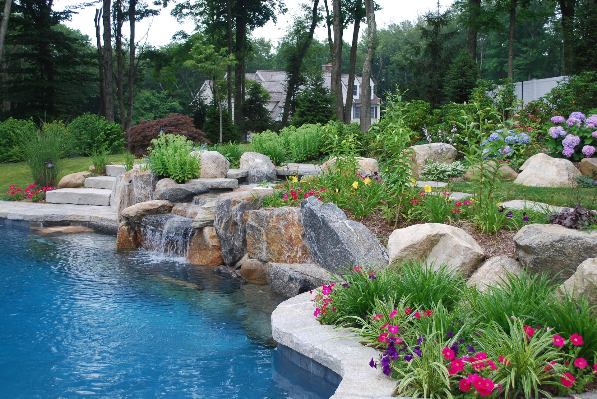 A swimming pool surrounded by rocks and flowers with a waterfall