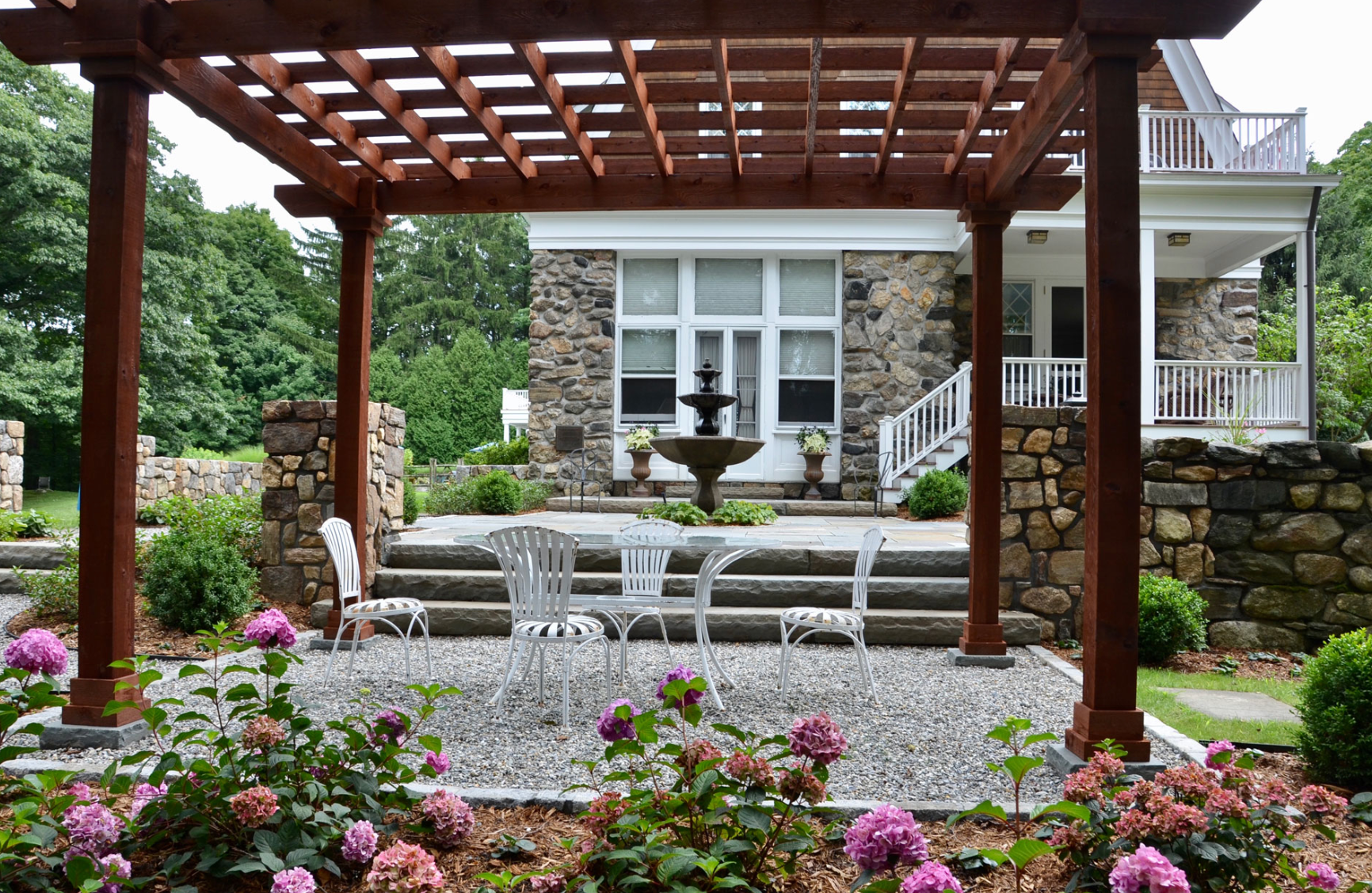 A pergola with a table and chairs underneath it in front of a house.