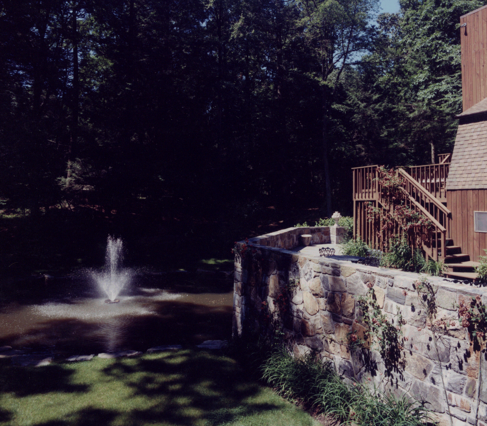 A stone wall surrounds a pond with a fountain in the middle