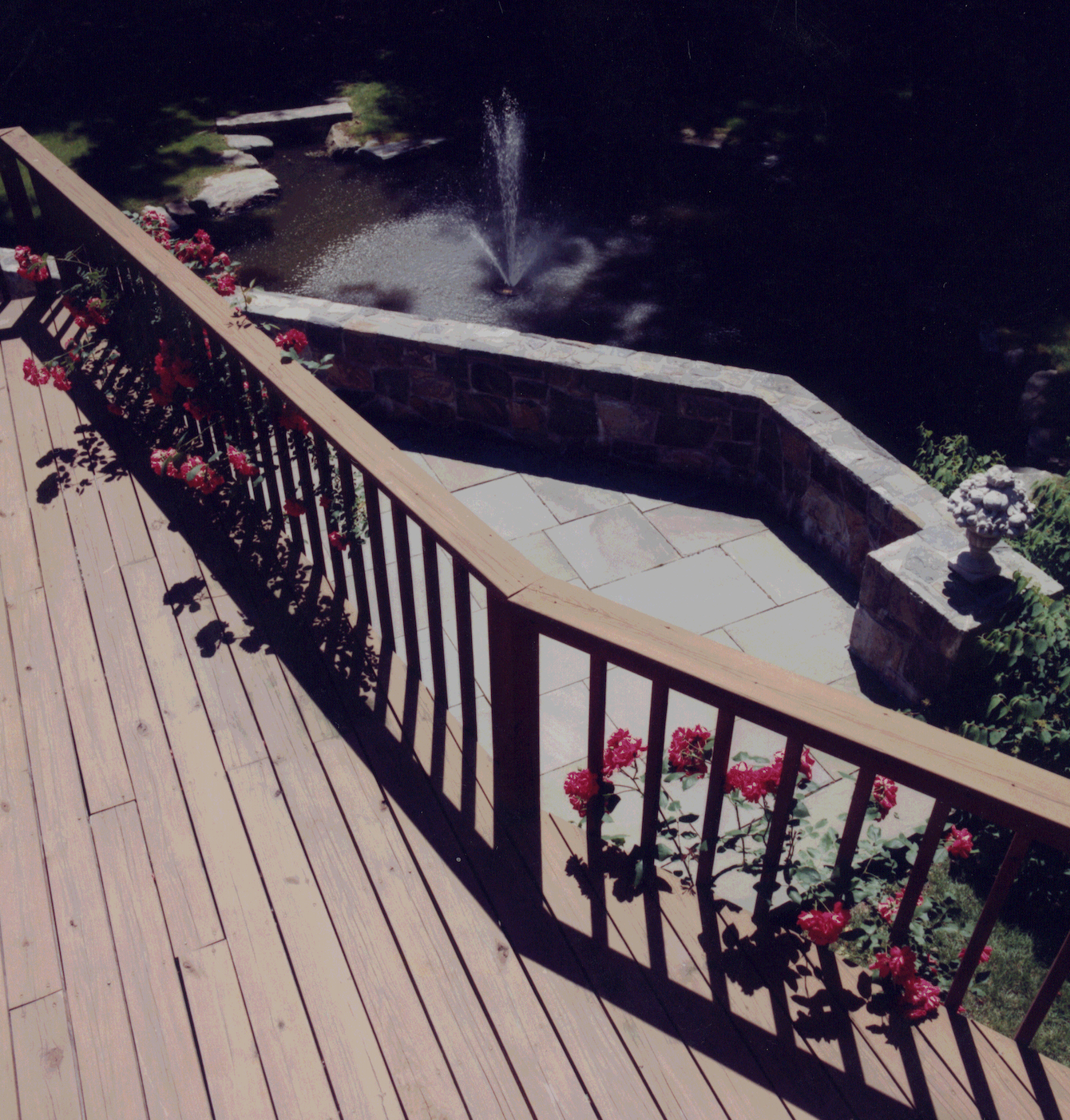 A wooden deck with flowers and a fountain in the background