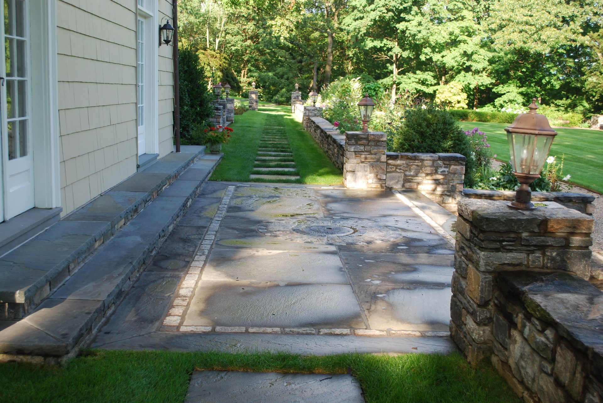 A stone walkway leading to a house with a stone wall