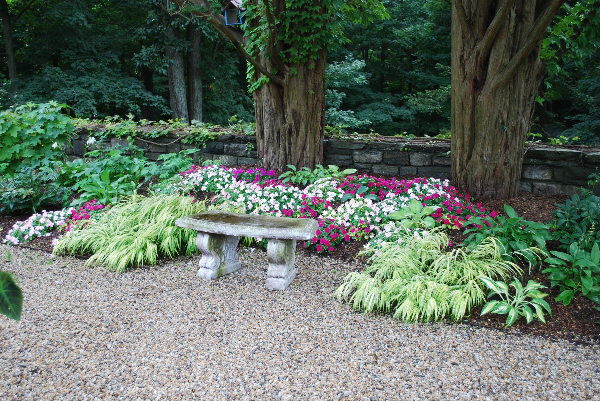 A stone bench is sitting in the middle of a garden surrounded by flowers.