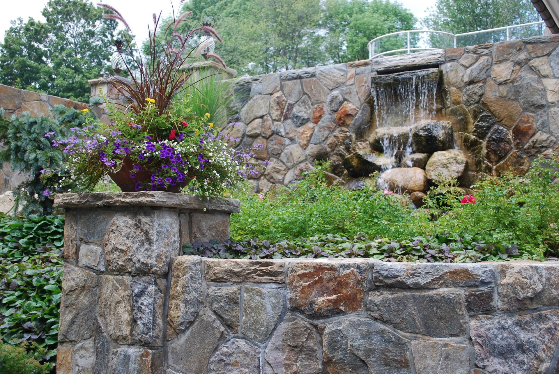 A stone wall with flowers and a waterfall in the background