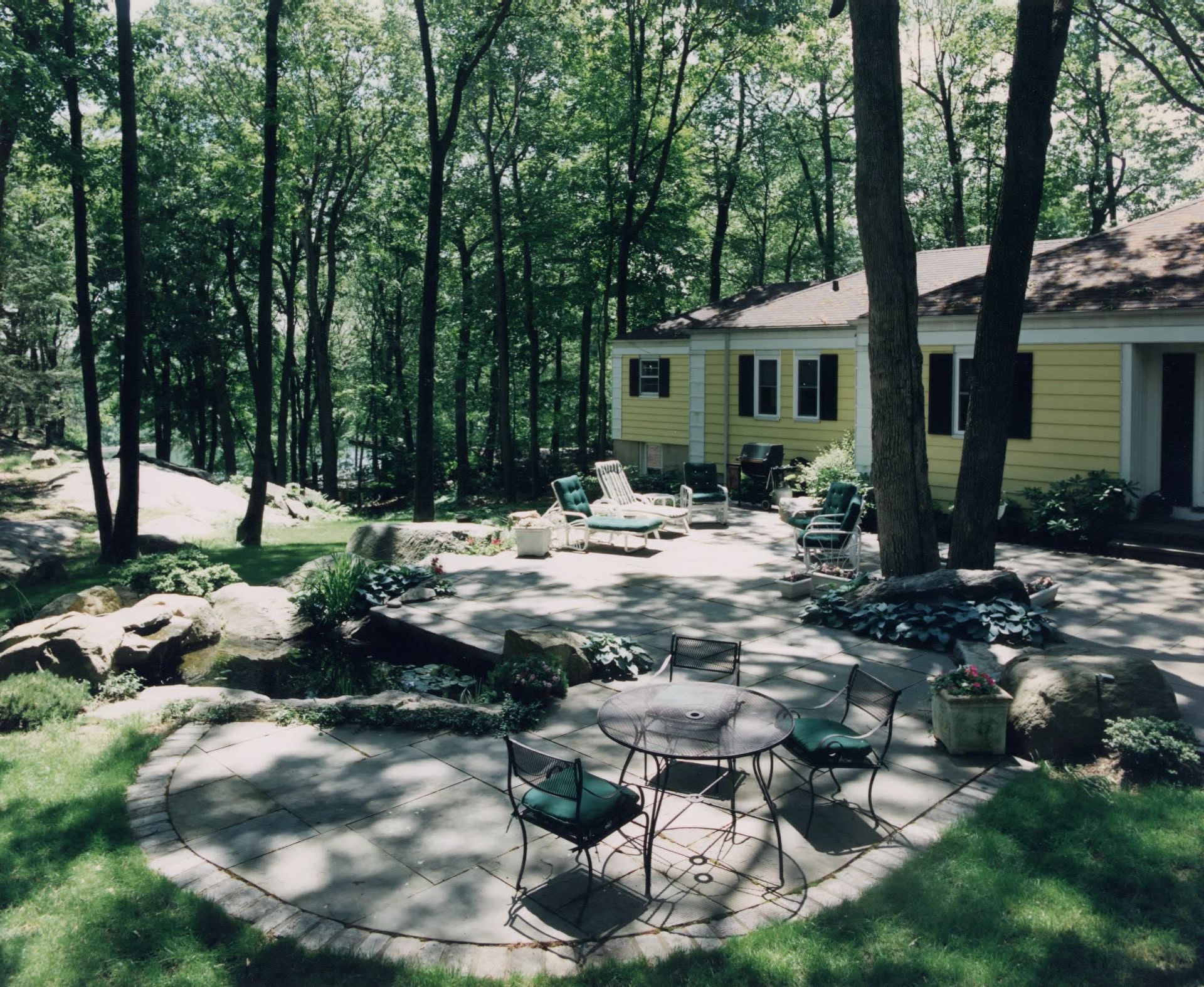 A patio with a table and chairs in front of a house in the woods