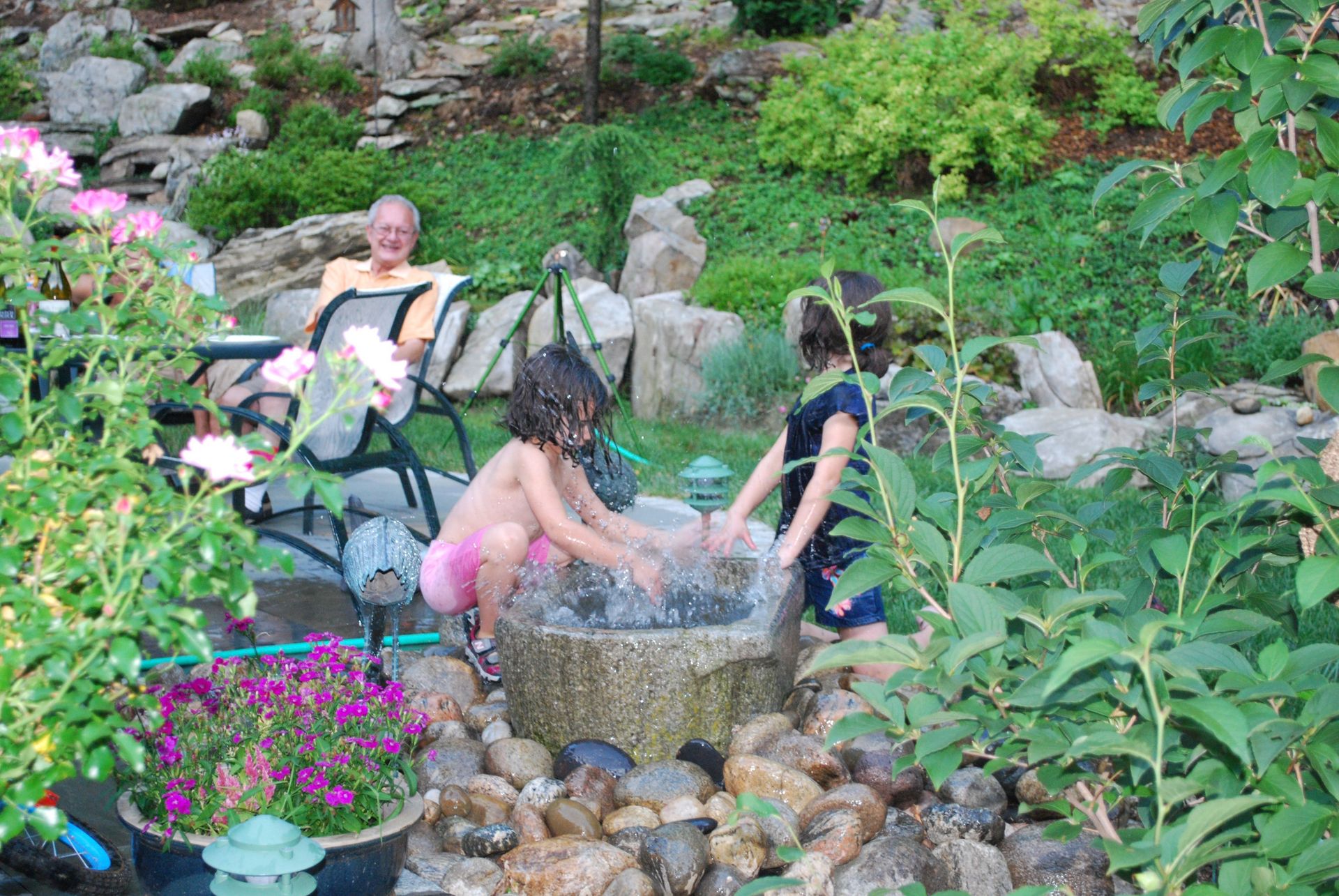 Two children are playing in a fountain in a garden.